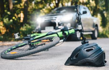 A bicycling helmet fallen on the asphalt next to a bicycle after an accident with a car.