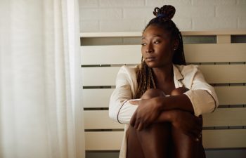 Young African American woman feeling sad and thinking of something while looking through the window at home. Copy space.